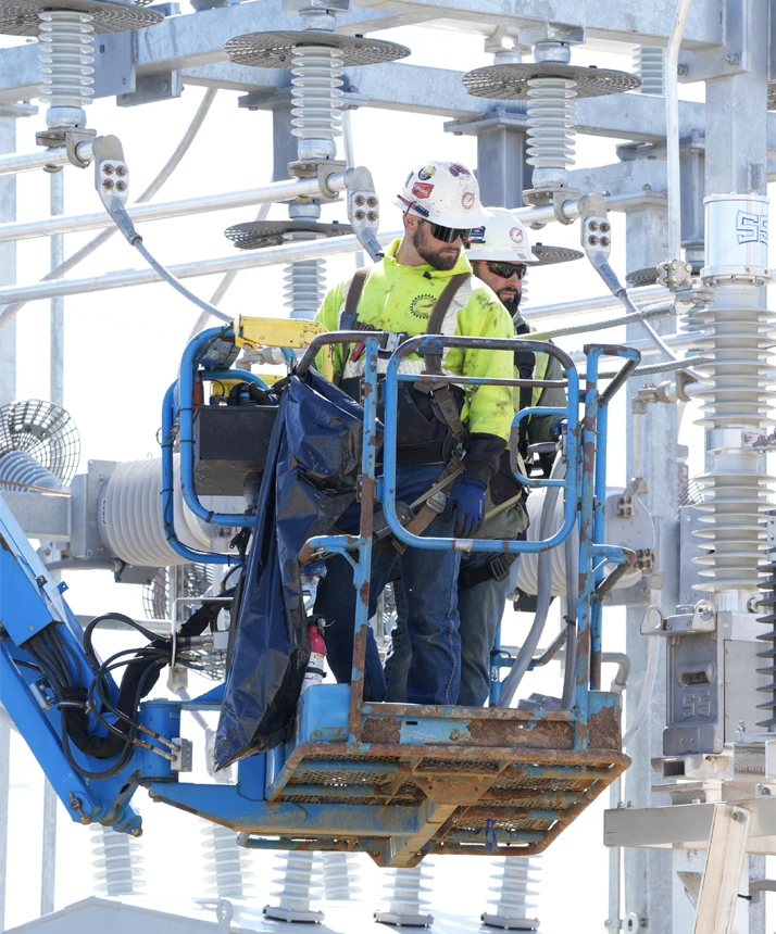 Motor City Electric technicians performing high-voltage electrical work on substation equipment using an elevated work platform.
